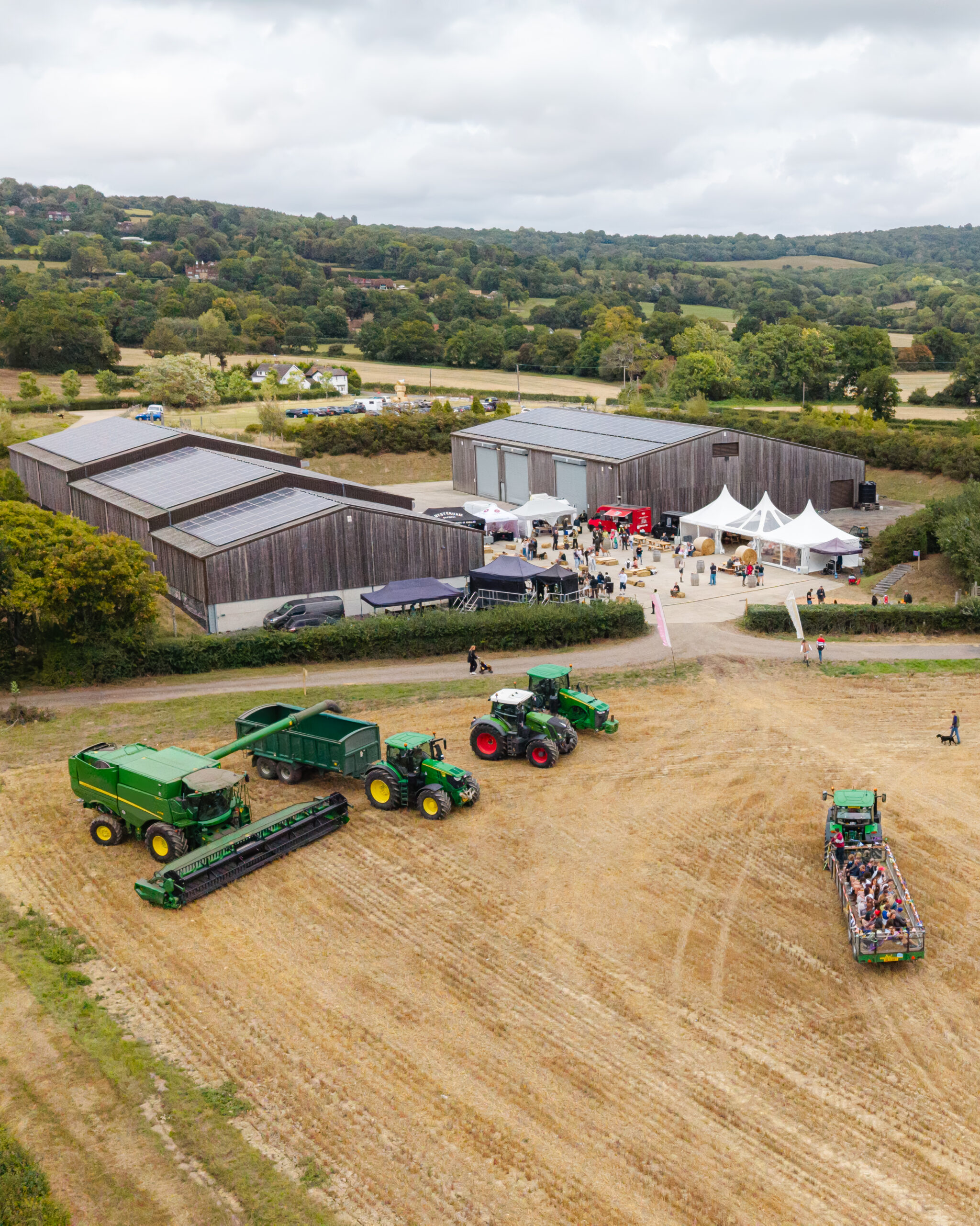 An aerial view of a farm yard in the kent countryside with a tractor and trailer in the foreground and festival tents and barns in the background